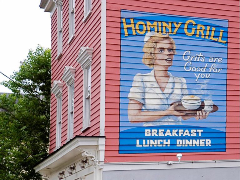 A mural on the building of the Hominy Grill Restaurant with a woman holding a steaming bowl below the words 'Grits are good for you'