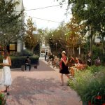 An artist's rendering of the proposed Gateway Walk Park and Liberty Center, a bricked walkway with outdoor cafe and people walking among many native plantings and trees